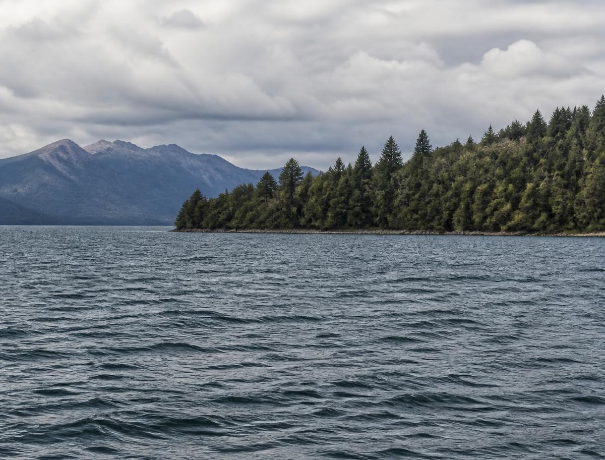 Wooden cabin beside a still lake surrounded by pines and mountains near Bariloche